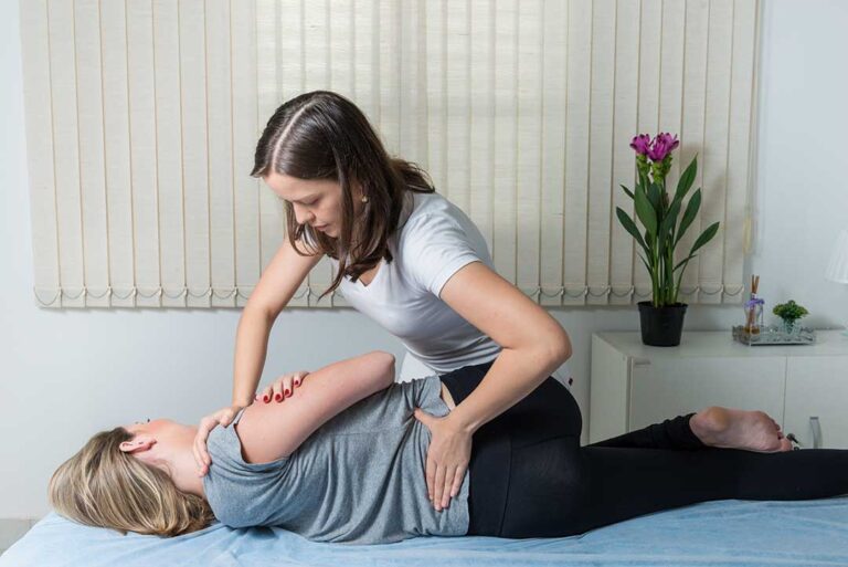 Person gently stretching the upper back beside a chair, with one hand supporting the neck.